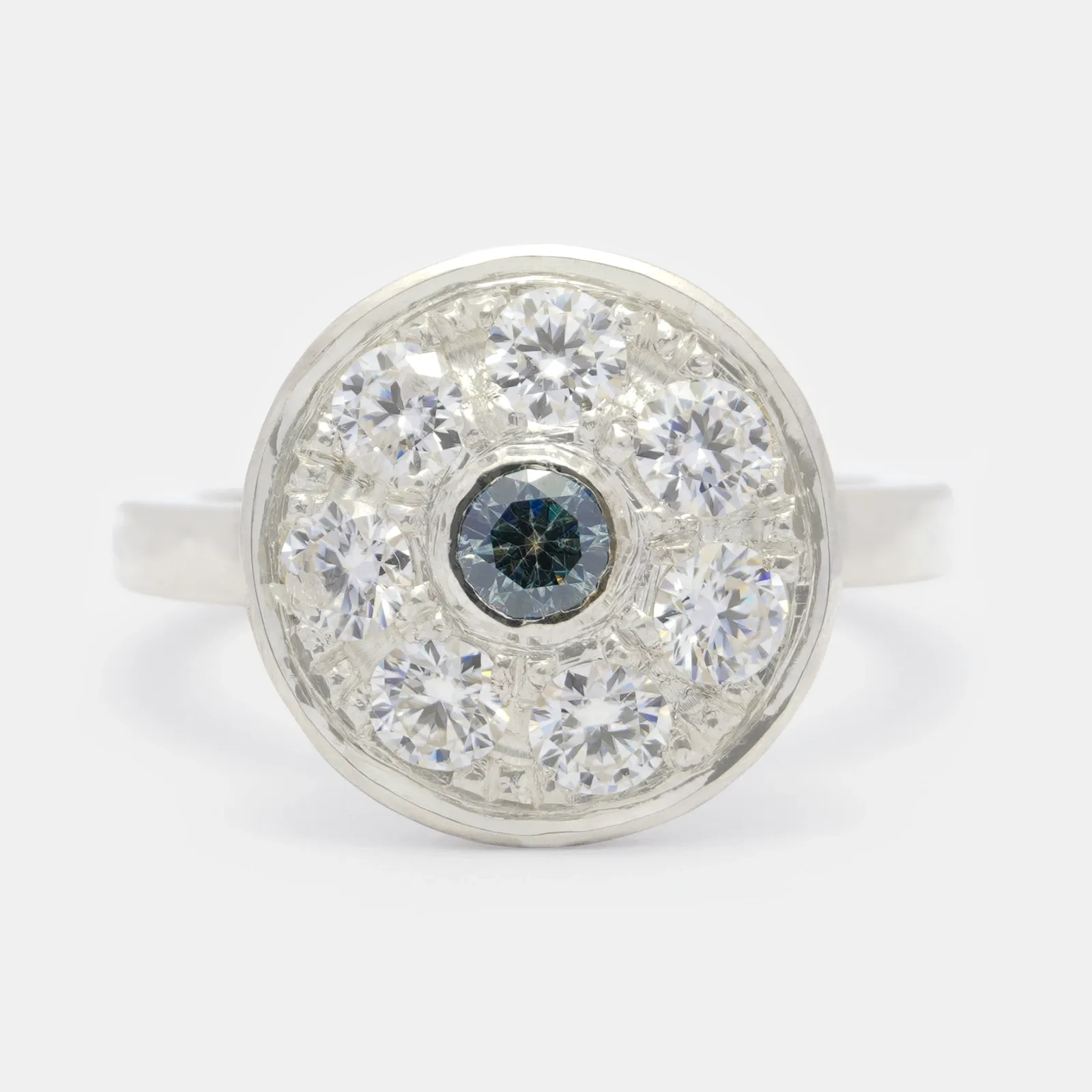 Anillo de plata visto de frente, con una cabeza redonda cubierta de piedras blancas y una piedra gris azulada engastada en bisel justo al centro.