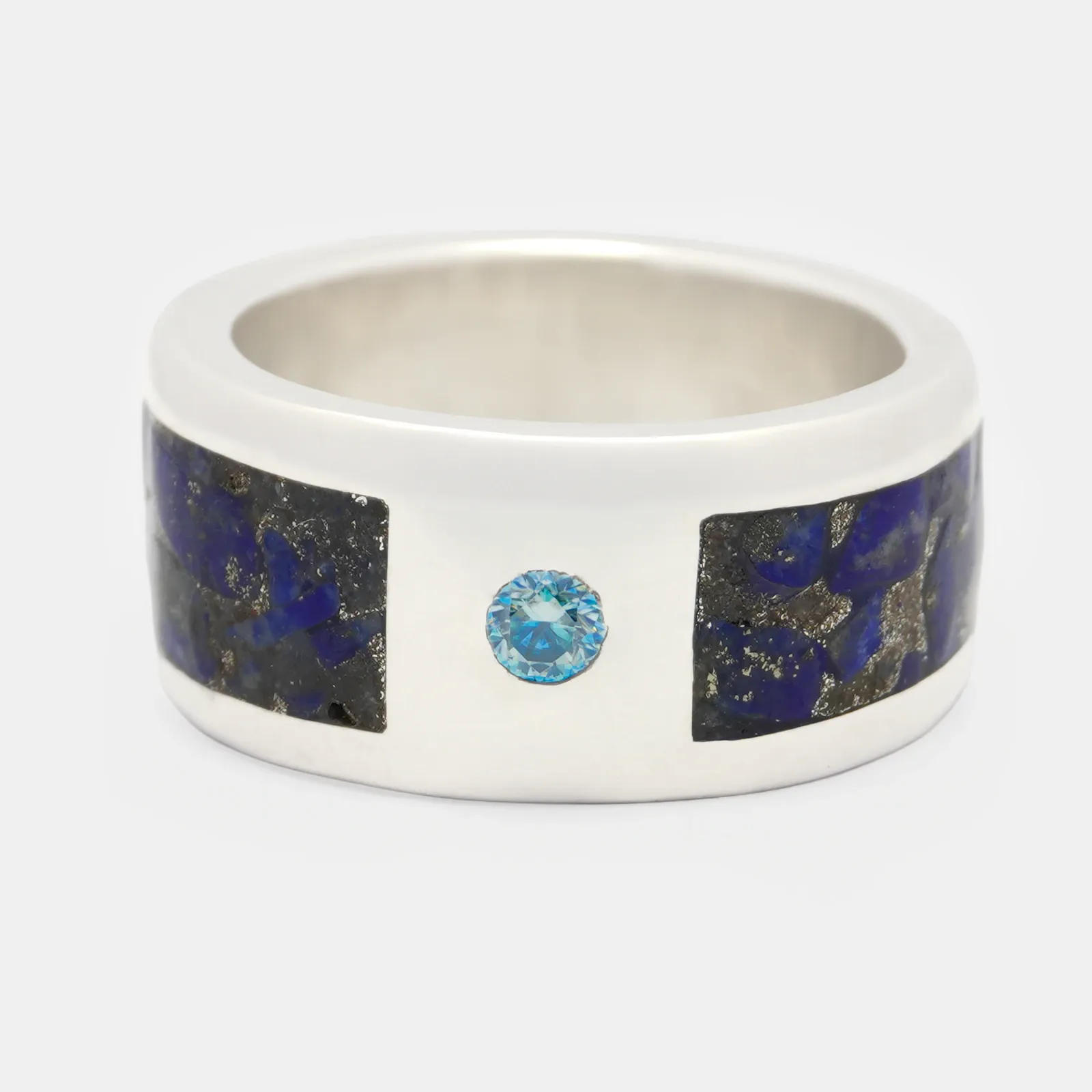 Anillo de plata de aro ancho visto de frente, con dos tramos de piedra azul incrustados a los lados y una piedra celeste redonda entre ambos.