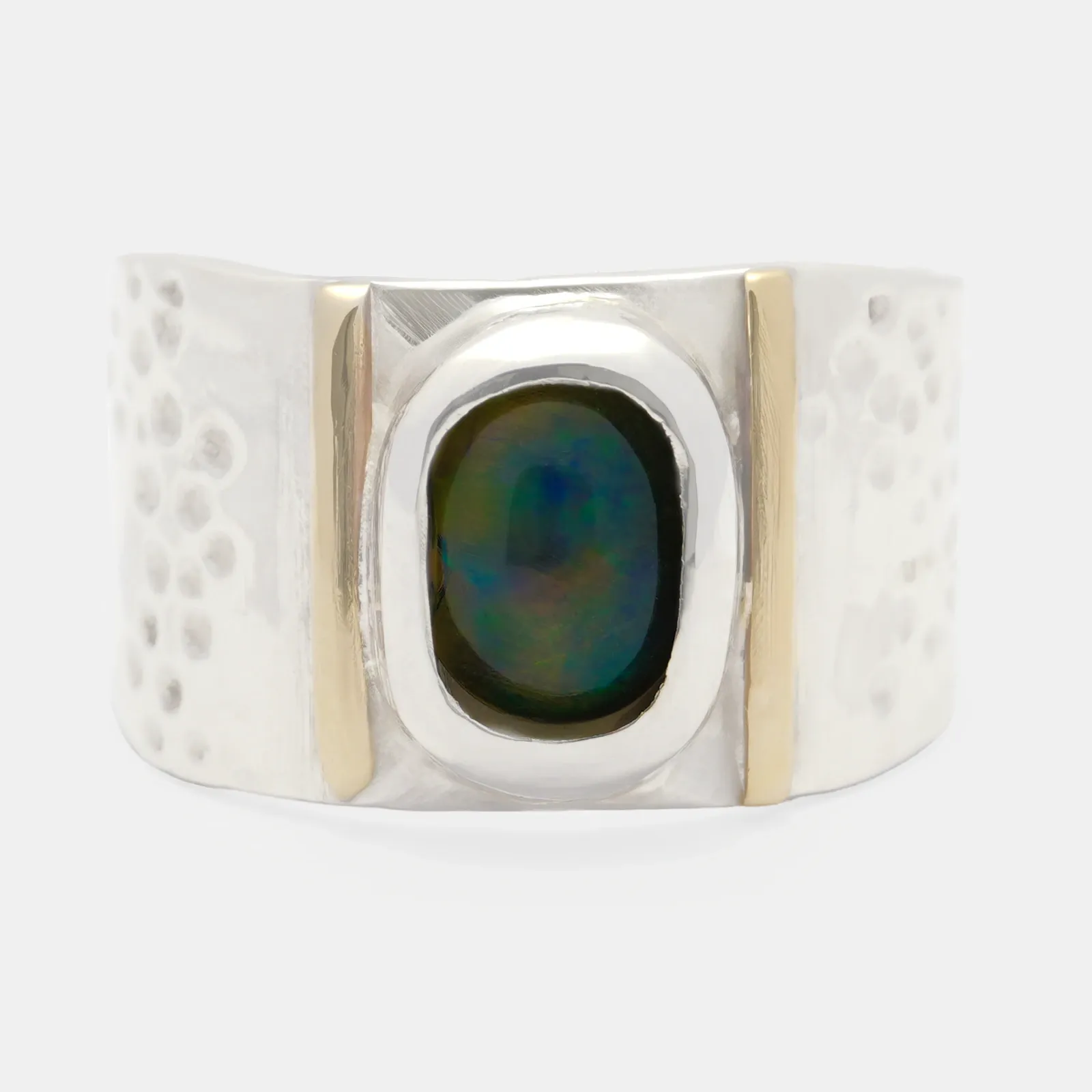 Anillo de plata de aro ancho visto de frente, con un ópalo ovalado de reflejos verdes y azules en un bisel liso, entre dos franjas verticales de brillo más cálido, y el resto de la superficie picada a martillo.